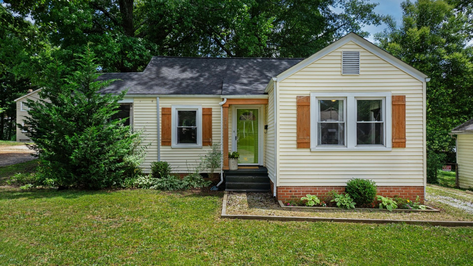 Small yellow house with green door, wooden shutters, and landscaped yard