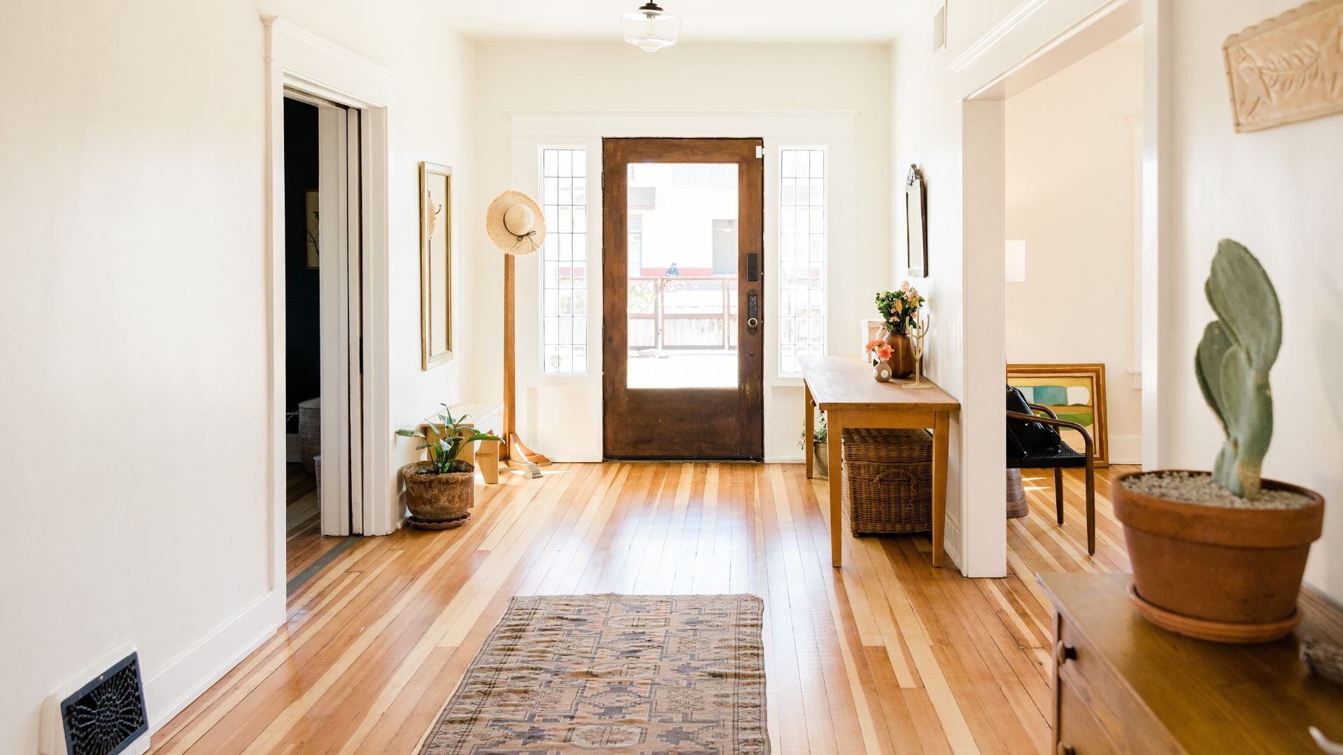 Bright entryway with wooden floor, straw hat, plants, and glass front door