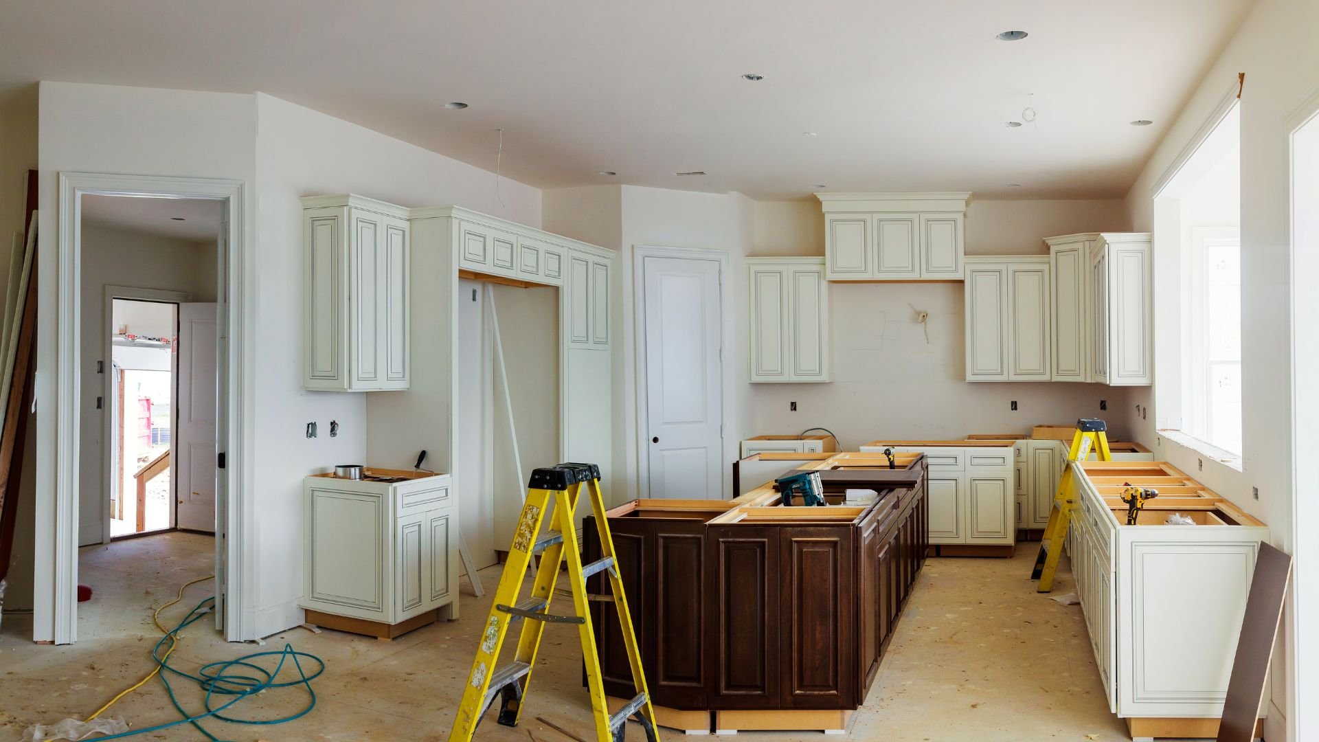 Kitchen renovation in progress with white cabinets and yellow ladders