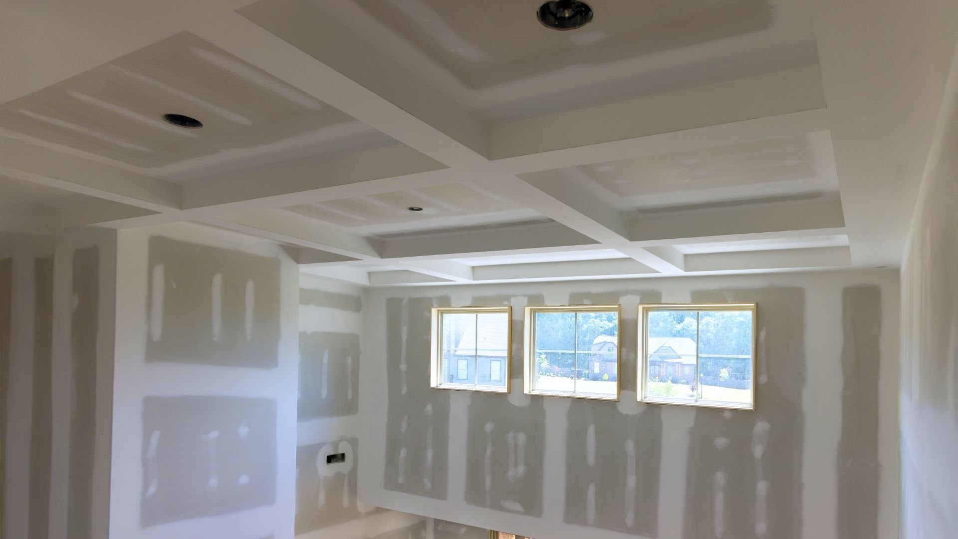 Unfinished room with drywall, coffered ceiling, and three windows