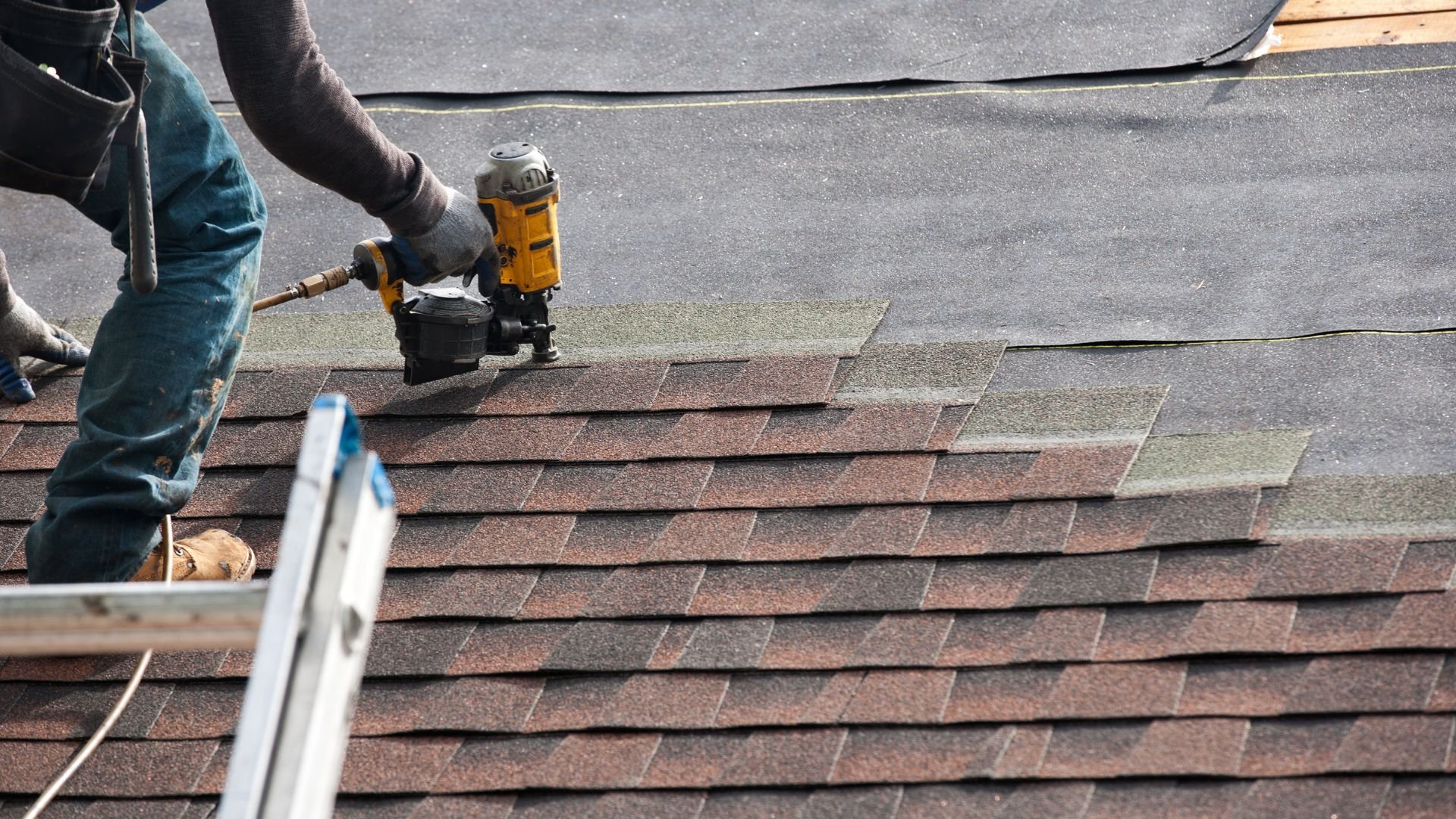 Roofing worker using nail gun to install shingles on residential roof