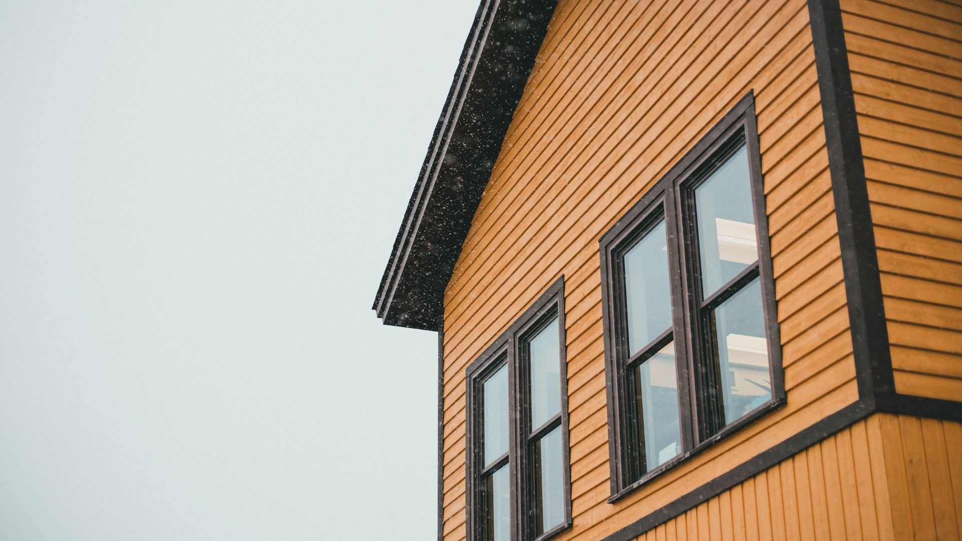 Yellow wooden house exterior with multiple windows against gray sky