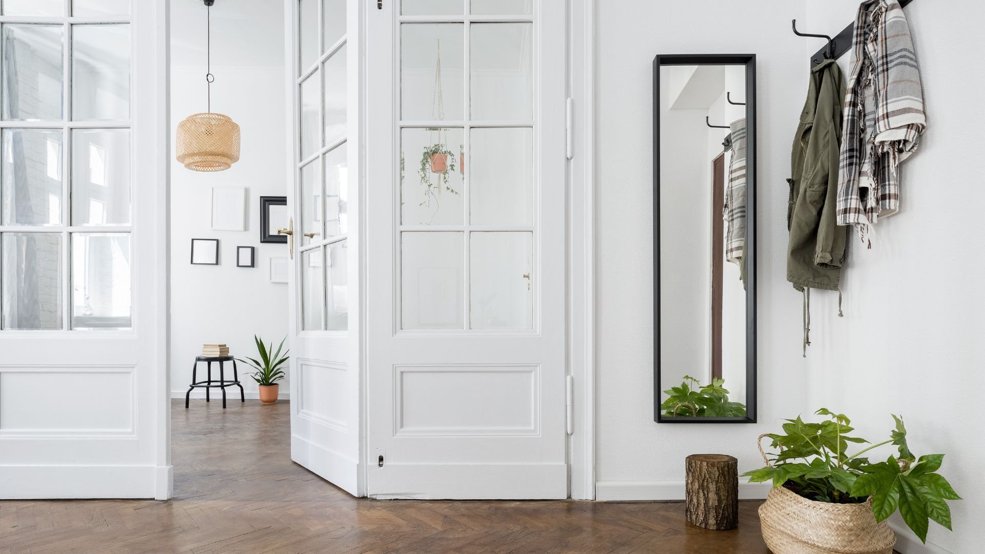 Bright entryway with white walls, plants, hanging lamp, and wooden floor